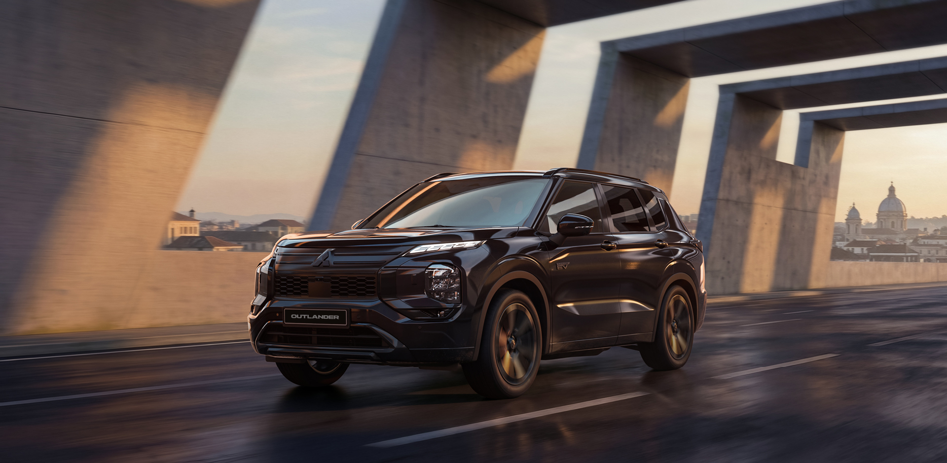 Schwarzer Mitsubishi Outlander Black in dynamischer Frontansicht unter einer modernen Betonbrücke bei Sonnenuntergang